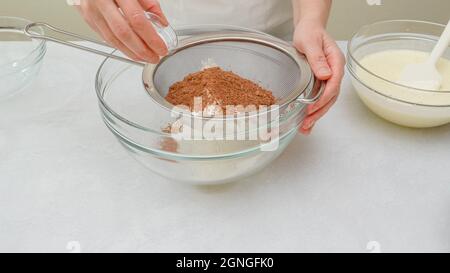 Torta al cioccolato ricetta passo per passo. Mescolare ingredienti secchi - farina, cacao in polvere, lievito in polvere - in un recipiente di vetro, vista ravvicinata Foto Stock