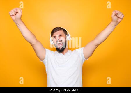 un uomo in cuffie bianche ascolta la musica e canta ad alta voce, alzando le mani. Foto Stock