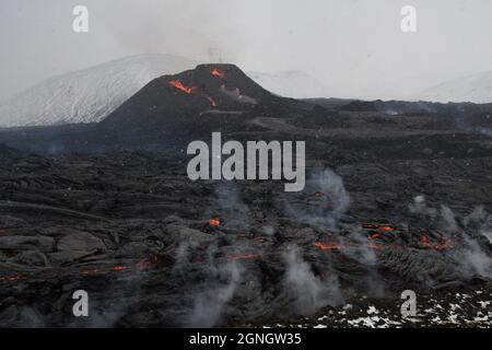 Due sfiati all'eruzione vulcanica di Fagradalfjall, Islanda. La lava nera crosta è in primo piano, con alcune macchie di lava rossa fusa e vapore che sale Foto Stock