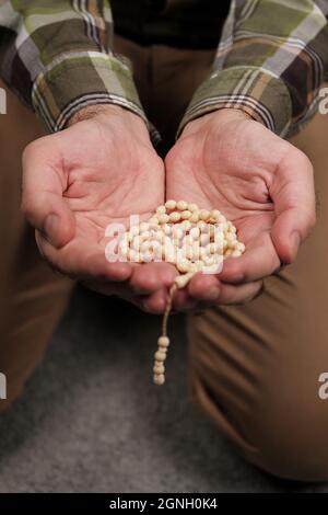 rosario nelle mani. uomo seduto con perline di preghiera color crema Foto Stock