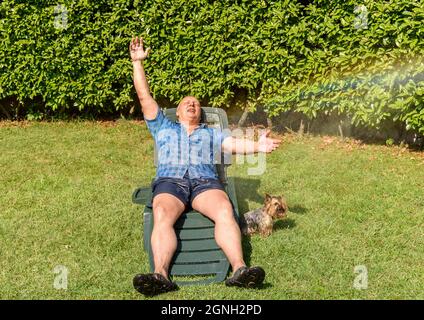 Uomo maturo con Yorkshire terrier cane sotto spruzzi d'acqua in giornata calda in giardino. Foto Stock