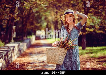 Sorridente ragazza rossa cammina da solo nel parco autunnale in una giornata calda di sole, mentre tiene la borsa indiana estate Foto Stock