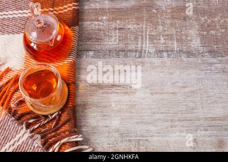 Tavolo da scrivania con plaid a scacchi, tazza da tè su sfondo di legno. Vista dall'alto, disposizione piatta, spazio di copia. Composizione autunnale. Foto Stock