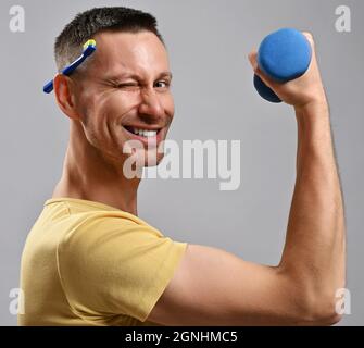 L'uomo adulto sorridente in t-shirt tiene lo spazzolino dietro l'orecchio e un manubello in mano guarda la macchina fotografica e i verricelli. Vista laterale Foto Stock