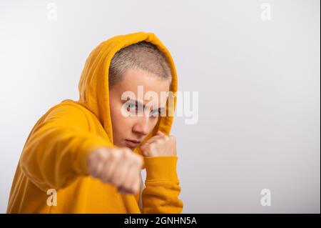 Giovane donna in cappa ocra che tiene i pugni vicino faccia su sfondo bianco. Boxer girl è pronta per una lotta. Foto Stock