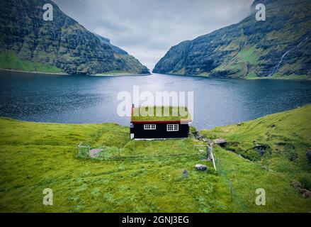 Vista estiva cupa del villaggio Saksun con tradizionale casa sul piano di un tappeto erboso. Meravigliosa scena serale di Pollurin Laguna, Isole Faroe, Regno di Danimarca, E. Foto Stock