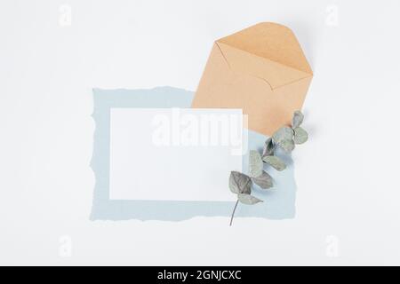 Mockup biglietto di auguri vuoto con busta e ramo verde eucalipto su sfondo bianco Foto Stock