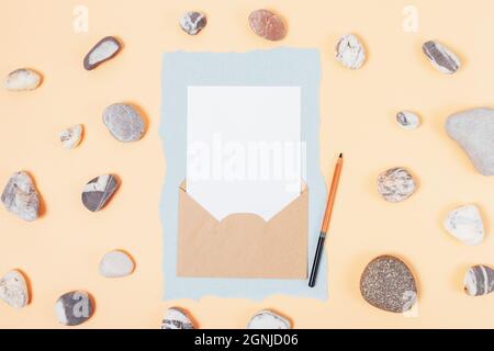 Mockup invito bianco in busta marrone su sfondo beige con pietre naturali, piatto Foto Stock