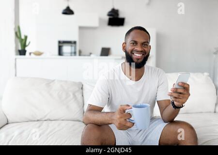 Uomo nero che texting sul suo smartphone bere caffè Foto Stock