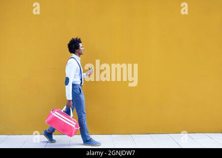 Uomo nero con acconciatura afro che porta una borsa sportiva e smartphone su sfondo giallo. Foto Stock