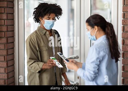 Lavoratore femminile con smartphone Scanning Digital Covid-19 certificato di vaccinazione del cliente Cafe Foto Stock