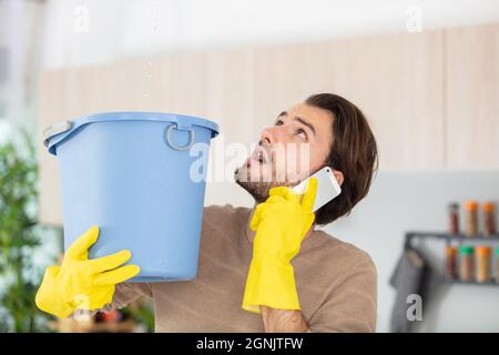 uomo preoccupato che chiama l'idraulico mentre l'acqua cade sul soffitto Foto Stock