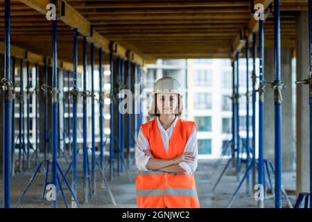 Ritratto di bella donna architetto che si erge folle e sorride sullo sfondo di edifici, all'aperto. Foto Stock