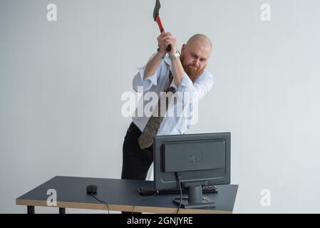 Stressato uomo d'affari pazzo che distrugge il suo computer in ufficio usando il concetto di problema dell'ascia. L'uomo ha problemi sul lavoro e la frustrazione. Foto Stock