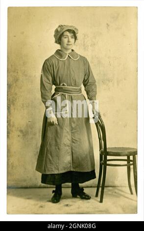 Cartolina originale dell'era della prima Guerra Mondiale del lavoratore di guerra di fabbrica femminile grazioso, che indossa una tunica e cappellino di mob, possibilmente lavoratore di munizioni, circa 1916, luogo sconosciuto, Regno Unito Foto Stock