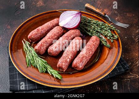 Kofta cruda carne kebabs salsicce su un piatto con erbe. Sfondo scuro. Vista dall'alto Foto Stock