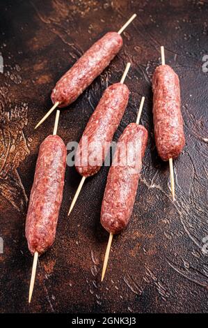 Kebab crudo di carne kofta salsicce su spiedini. Sfondo scuro. Vista dall'alto Foto Stock