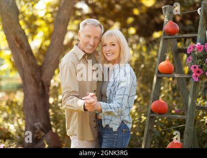 Una coppia anziana che ama ballare in giardino il giorno d'autunno soleggiato, riposandosi insieme all'aperto e sorridendo alla macchina fotografica Foto Stock