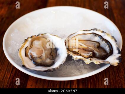 Due ostriche fresche e aperte si trovano su un piatto di ghiaccio. Frutti di mare, afrodisiaci Foto Stock