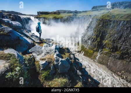 Donna viaggiatore alla scogliera bordo cascata Dettioss in Islanda nord-orientale. Detifoss è una cascata del Parco Nazionale Vatnajokull, che si è sempre più notata Foto Stock