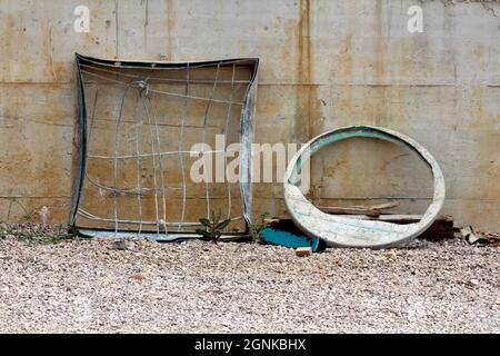 Telaio in metallo per tombini intrecciato vecchio e molto usato, riempito con una rete di filo resistente accanto a rotto, sporco, coperchio in plastica verde per tombini lasciati sulla ghiaia Foto Stock