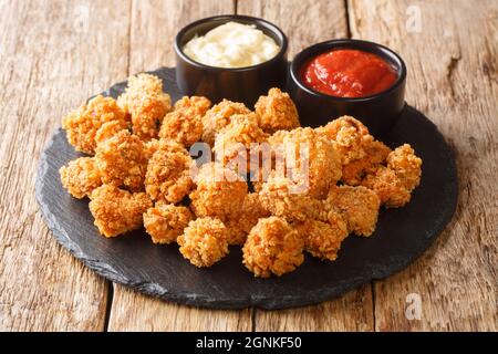I popcorn di pollo sono piccole fette di pollo che erano impanate e fritte in primo piano nel piatto di ardesia sul tavolo. Orizzontale Foto Stock