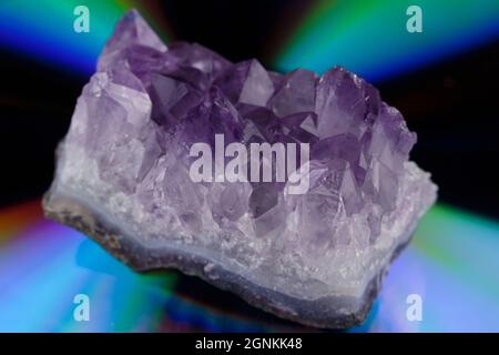 un cristallo di roccia di ametista viola grezzo su uno sfondo psichedelico, iridescente, colorato con profondità di campo bassa Foto Stock