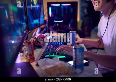 Ragazzo adolescente di bere caffeina Energy Drink Gaming a casa utilizzando due schermi di computer di notte Foto Stock