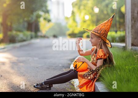 Ritratto lifestyle di ragazza caucasica felice con capelli biondi sette anni in costume arancione nero di cui celebra Halloween da solo Foto Stock