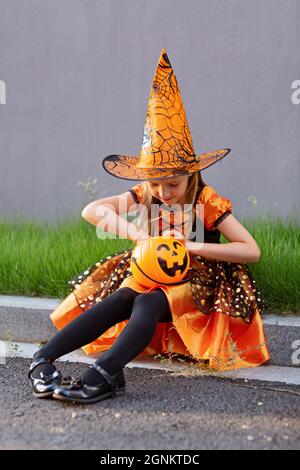 Ritratto lifestyle di ragazza caucasica felice con capelli biondi sette anni in costume arancione nero di cui celebra Halloween da solo Foto Stock