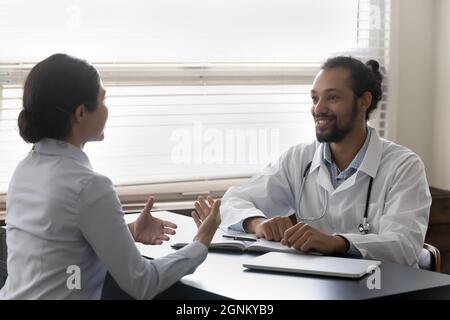 Felice ottimista giovane medico ascoltando paziente su appuntamento Foto Stock