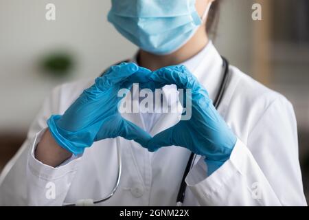 Medico in maschera facciale, guanti protettivi in lattice che mostrano il cuore del dito Foto Stock