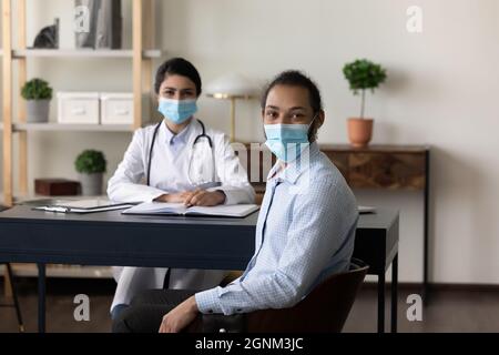 Felice medico multietnico femminile e paziente maschile che indossa maschere per il viso Foto Stock