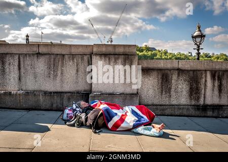 Londra, 22 settembre 2021: Una persona senza tetto avvolta nella bandiera sindacale che dorme sulla riva sud del Tamigi a Lambeth, Londra Foto Stock