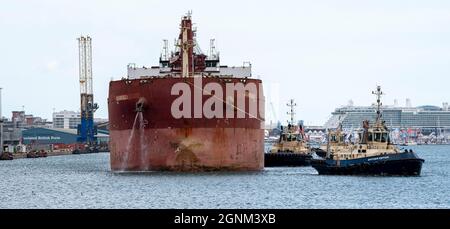 Southampton, Inghilterra, Regno Unito, 2021. Tugs scorta un portarinfuse che naviga vuoto nel porto di Southampton. Passando accanto alle navi da crociera. Foto Stock