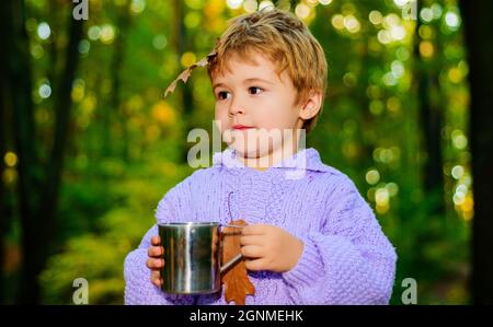 Bellissimo bambino in maglione con bevanda calda in autunno foresta. Ora di autunno. Carino bambino nel parco autunnale. Buona infanzia. Ragazzo su sfondo naturale autunno. Foto Stock