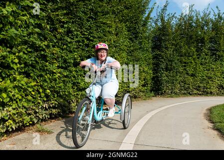 Hakendover, Brabante fiammingo, Belgio - 09 20 2021: Donna di 39 anni con sindrome Down sulla strada con il suo triciclo Foto Stock