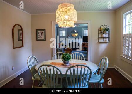 Una piccola sala da pranzo con un'illuminazione in rattan di tendenza e un tavolo da pranzo dipinto di blu Foto Stock