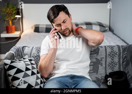 Uomo in schiuma collo cervicale sta chiamando al telefono alla compagnia di assicurazione per assistenza medica dopo l'incidente, sensazione di dolore al collo, lesioni e. Foto Stock