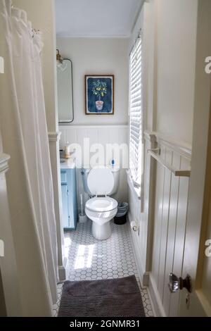 Una piccola stanza da bagno per gli ospiti con un vanity blu vintage, specchio nero retrò, e vetro chiaro lampada in un cottage a noleggio a breve termine recentemente rinnovato Foto Stock