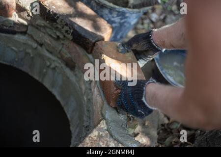 Un lavoratore depone la bocca di un pozzo settico di mattoni. Lavorare con cemento. Foto Stock