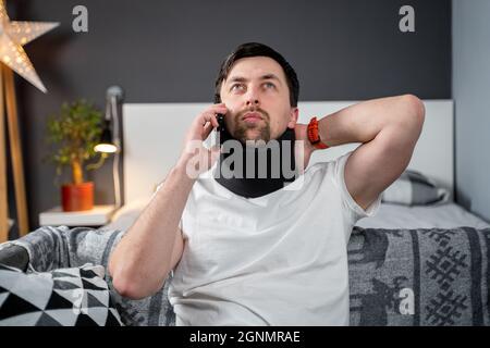 Uomo in schiuma collo cervicale sta chiamando al telefono alla compagnia di assicurazione per assistenza medica dopo l'incidente, sensazione di dolore al collo, lesioni e. Foto Stock