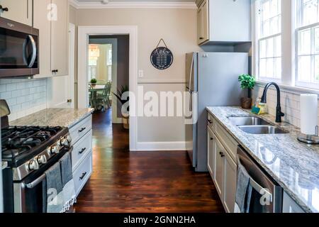 Una piccola cucina cottage con armadi grigi e pavimenti in legno scuro in una casa di affitto a breve termine Foto Stock