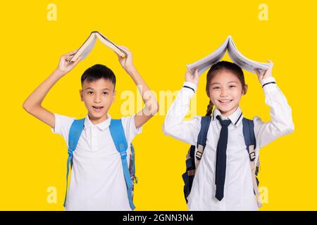 Felice ragazzo studente e ragazza che tiene libro su head.Isolated su sfondo giallo. Foto Stock