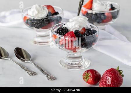 Piatti in vetro da dessert ripieni di frutti di bosco e panna leggera pronti per mangiare. Foto Stock