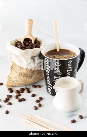 Una tazza di caffè con fuoco selettivo posto sulla parola caffè con un sacco di fagioli dietro e crema davanti. Foto Stock