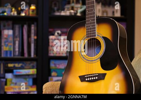 Classica chitarra a corda gialla e marrone contro blurred libreria da parete a casa. Elemento di progettazione. Strumento musicale, apprendimento dell'arte e background interno. Foto Stock