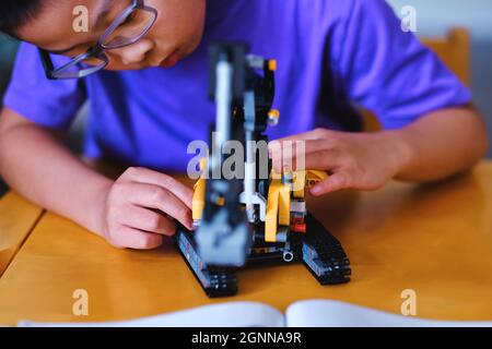 Bambino ragazzo costruzione meccanico Lego mattoni technic blocchi set sul tavolo a casa durante la pausa estiva. Scienza infantile, innovazione, ingegneria e creatività. Foto Stock