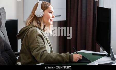 Giovane donna, disegnatrice di grafica, freelance, si è occupata di lavorare in remoto da casa utilizzando computer pc e tablet grafici in interni di salotto. Adolescente informale Foto Stock