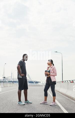 Coppie sportive africane che si parlano tra loro durante la loro riunione all'aperto, discutono di esercizi sportivi Foto Stock
